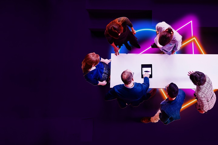 Colleagues stand around a table, assessing a document.