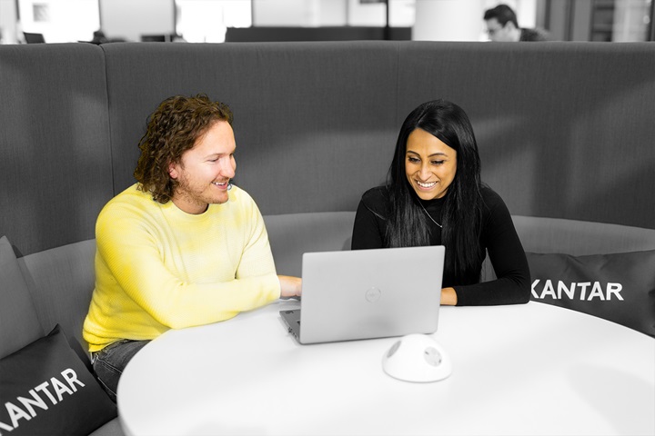 A black and white picture, with the man and woman at a pod in colour. The colleagues are looking at a laptop. 